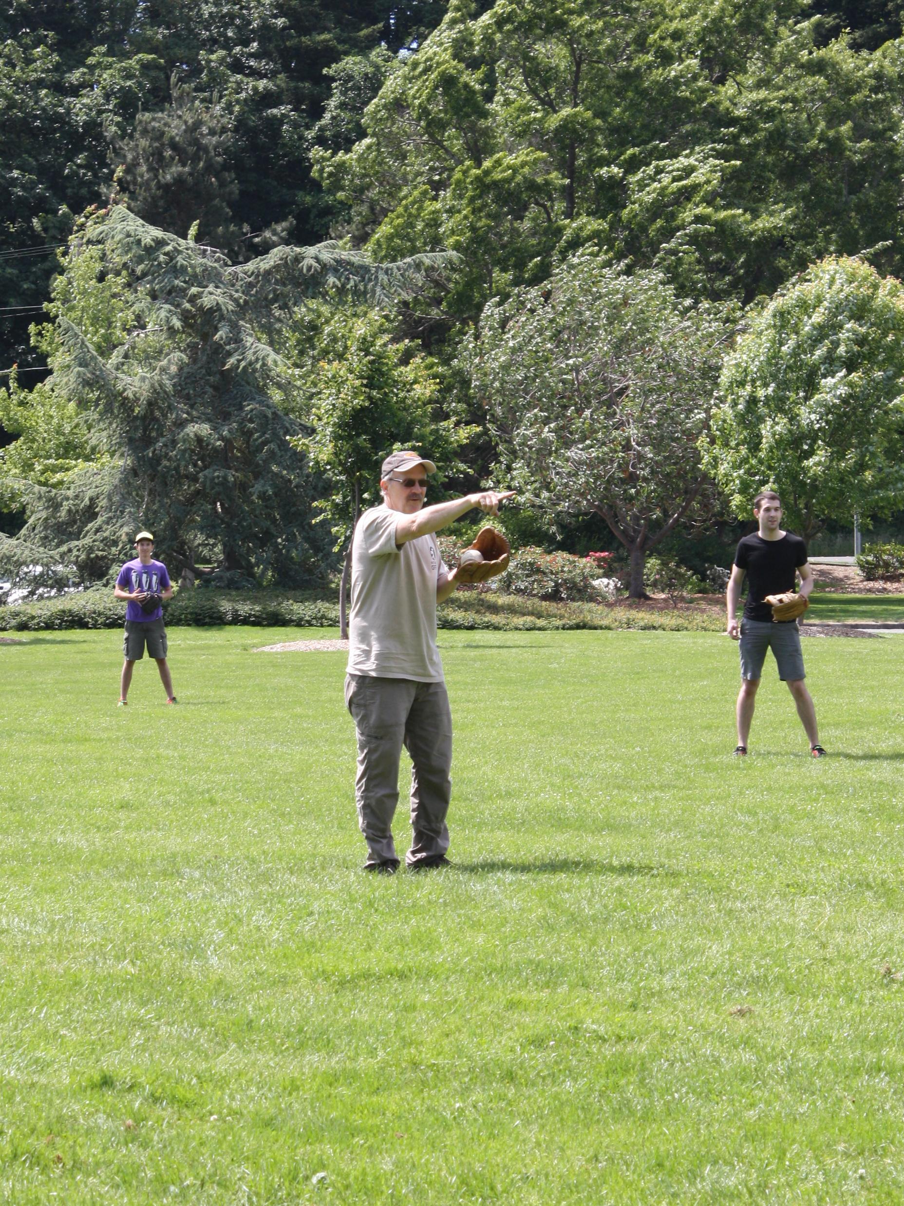 Professor John Harris takes the role of pitcher at a baseball game in the park.