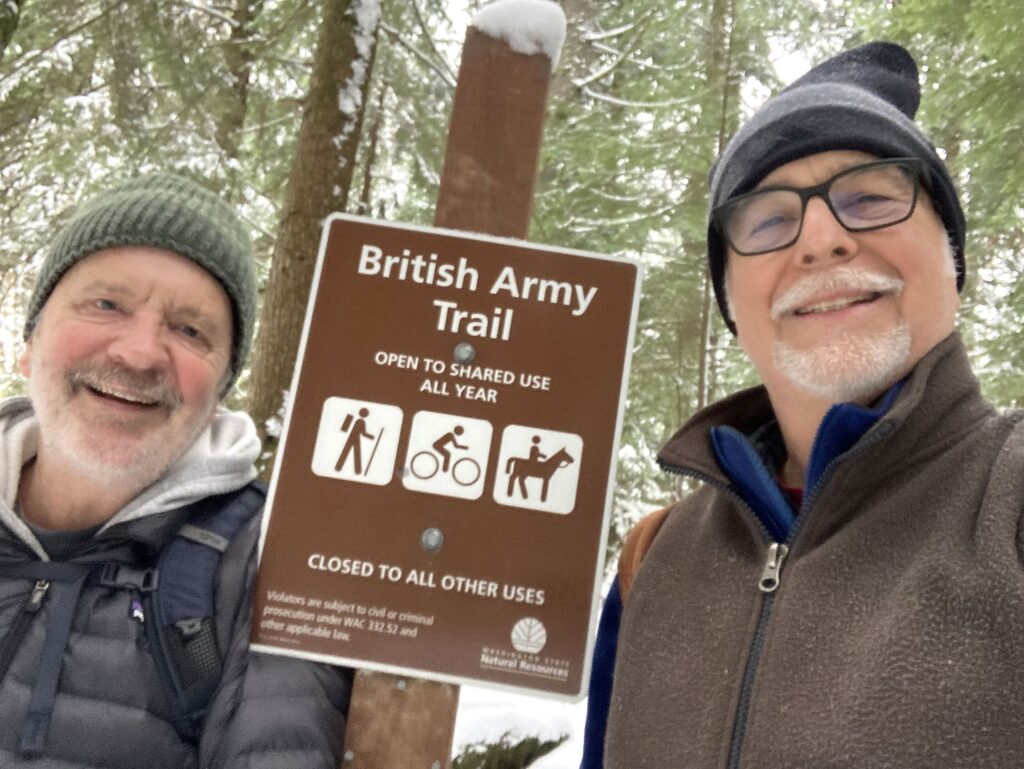 Scott Terrell and John Harris of Western Washington University's journalism department pose for a selfie on the snowy trail. Between then is a sign for the British Army Trail.