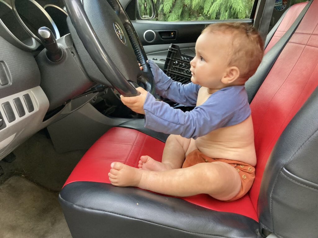 toddler sitting in the driver's side of a truck while holding onto the steering wheel.