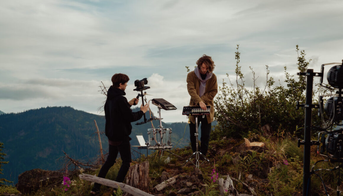Connor Jalbert films a musician playing on a grassy hill on the set of a video shoot for "In the Cascades."
