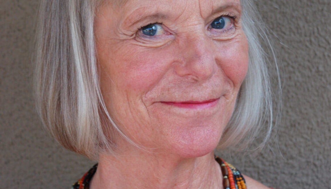 Portrait of a smiling Carolyn Dale, with a red shirt and matching necklace.