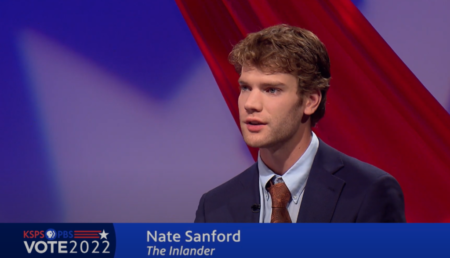 Nate Sanford appears on television for The Inlander during election season. Sanford has a red, white and blue background behind him and wears a tie.