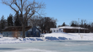 A frozen body of water with a blue snow-dusted house in the background.