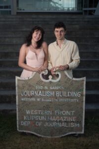 Audra Anderson and Ian Haupt hold the traditional "Journalism Building" sign. The stand behind the roughly 4-foot sign, which is covered in the signatures of former staff members.