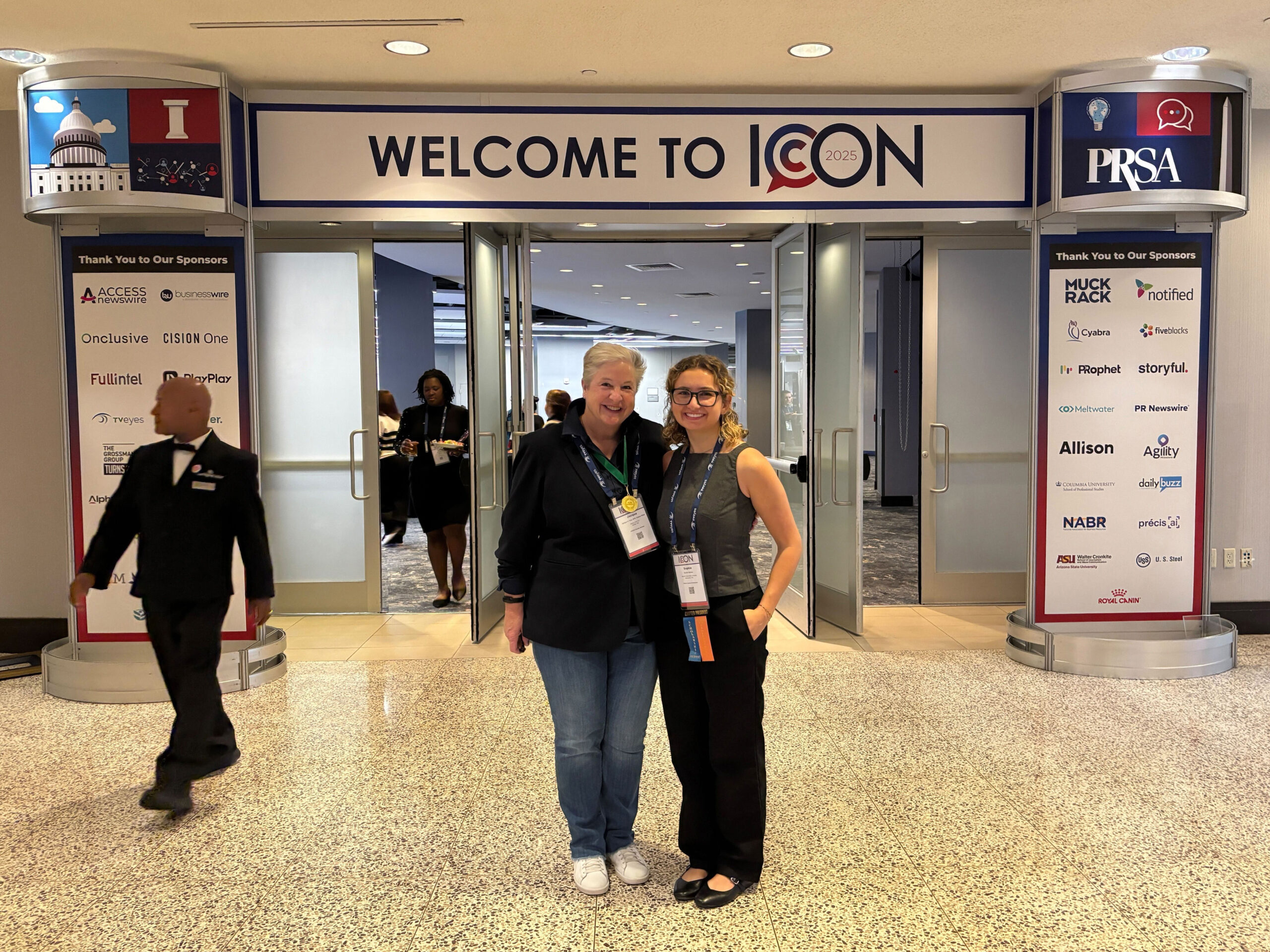 Two women smile at a convention entrance under a "WELCOME TO ICON 2025" sign, with sponsor logos displayed.
