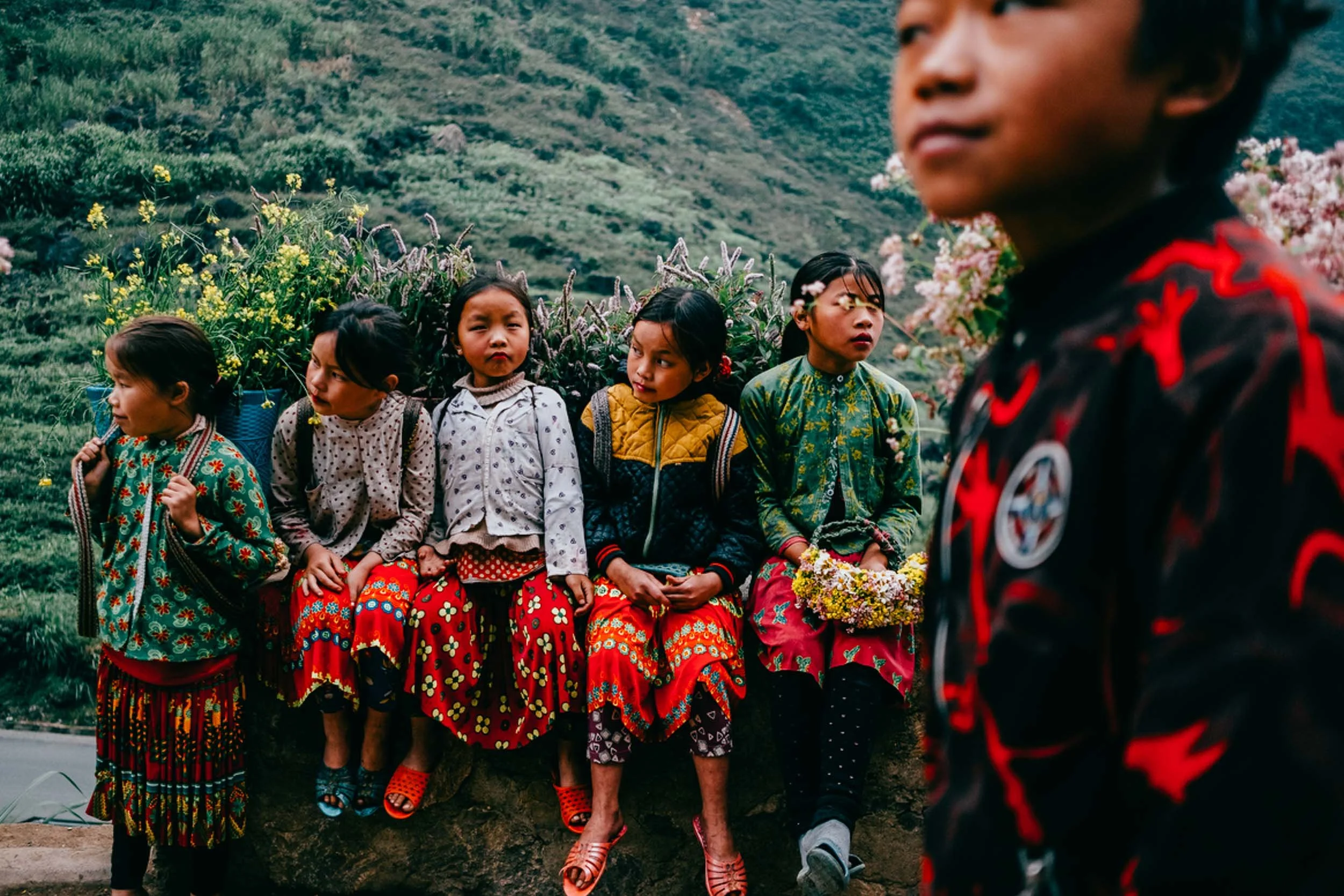 Children sit on the side of a road with backpacks full of plants. // Photo by Jake Parrish