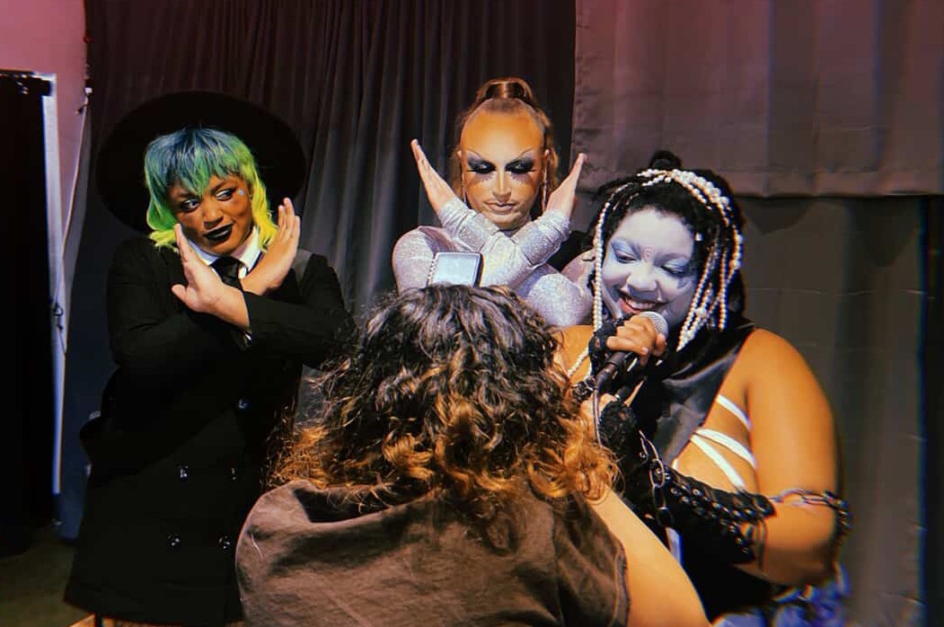 Three people pose with their hands around their face for a photographer.